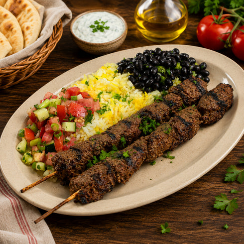 Platter of beef skewers side of rice, black beans, and chop-chop on a wooden table.
