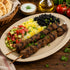 Platter of beef skewers side of rice, black beans, and chop-chop on a wooden table.